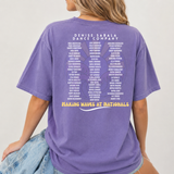 Purple t-shirt with text on the back worn by a person, against a plain background