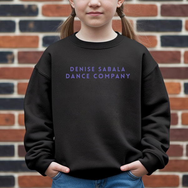 Child wearing a black sweatshirt with 'Denise Sabala Dance Company' text in front of a brick wall.