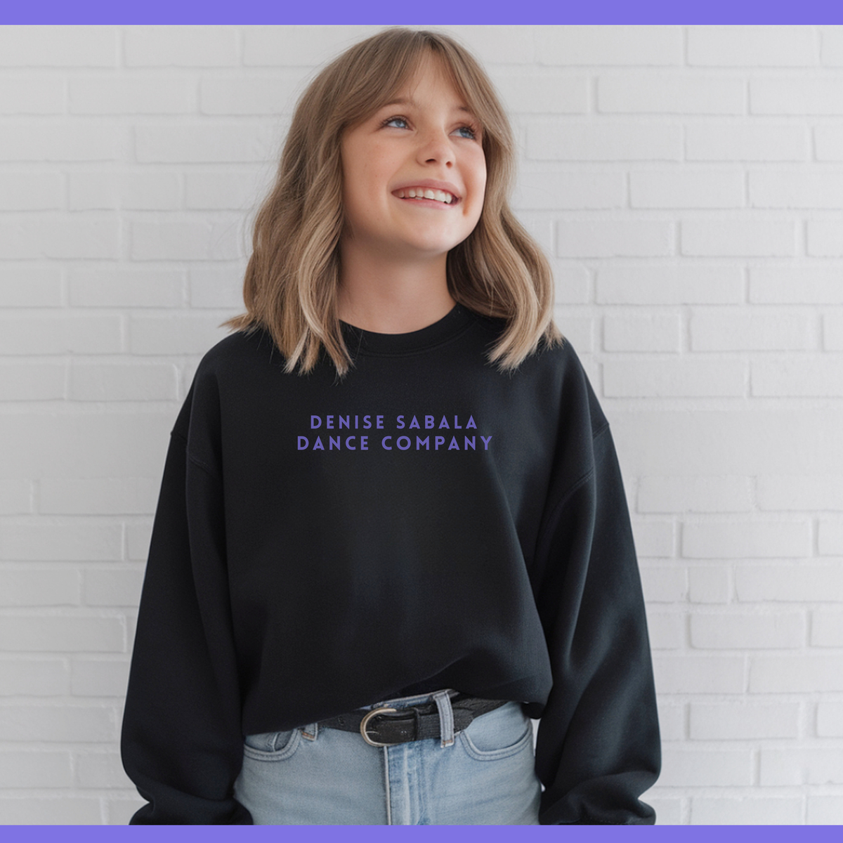 Person wearing a black sweatshirt with 'Denise Sabala Dance Company' text against a white brick wall.