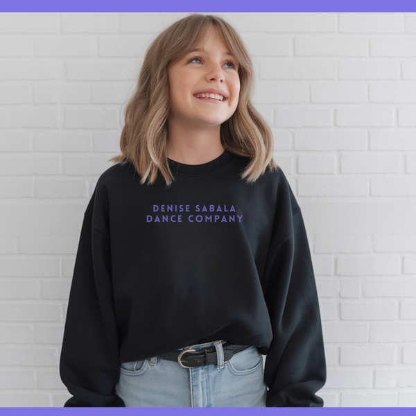 Person wearing a black sweatshirt with 'Denise Sabala Dance Company' text against a white brick wall.