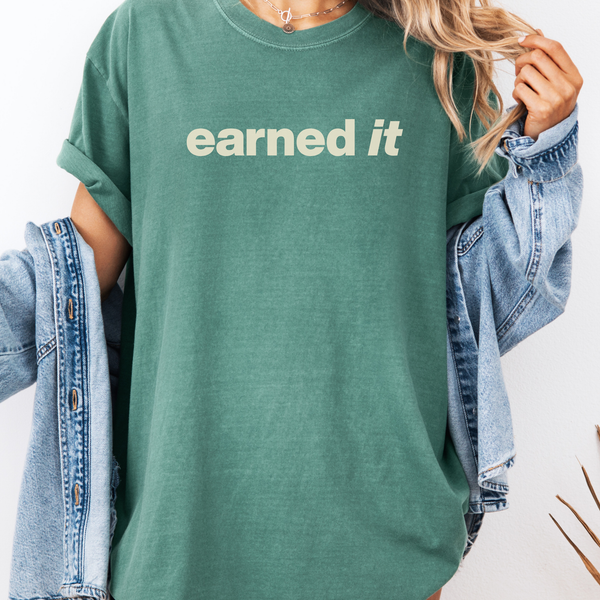 A woman in  a light green tee shirt that says "earned it" in beige standing