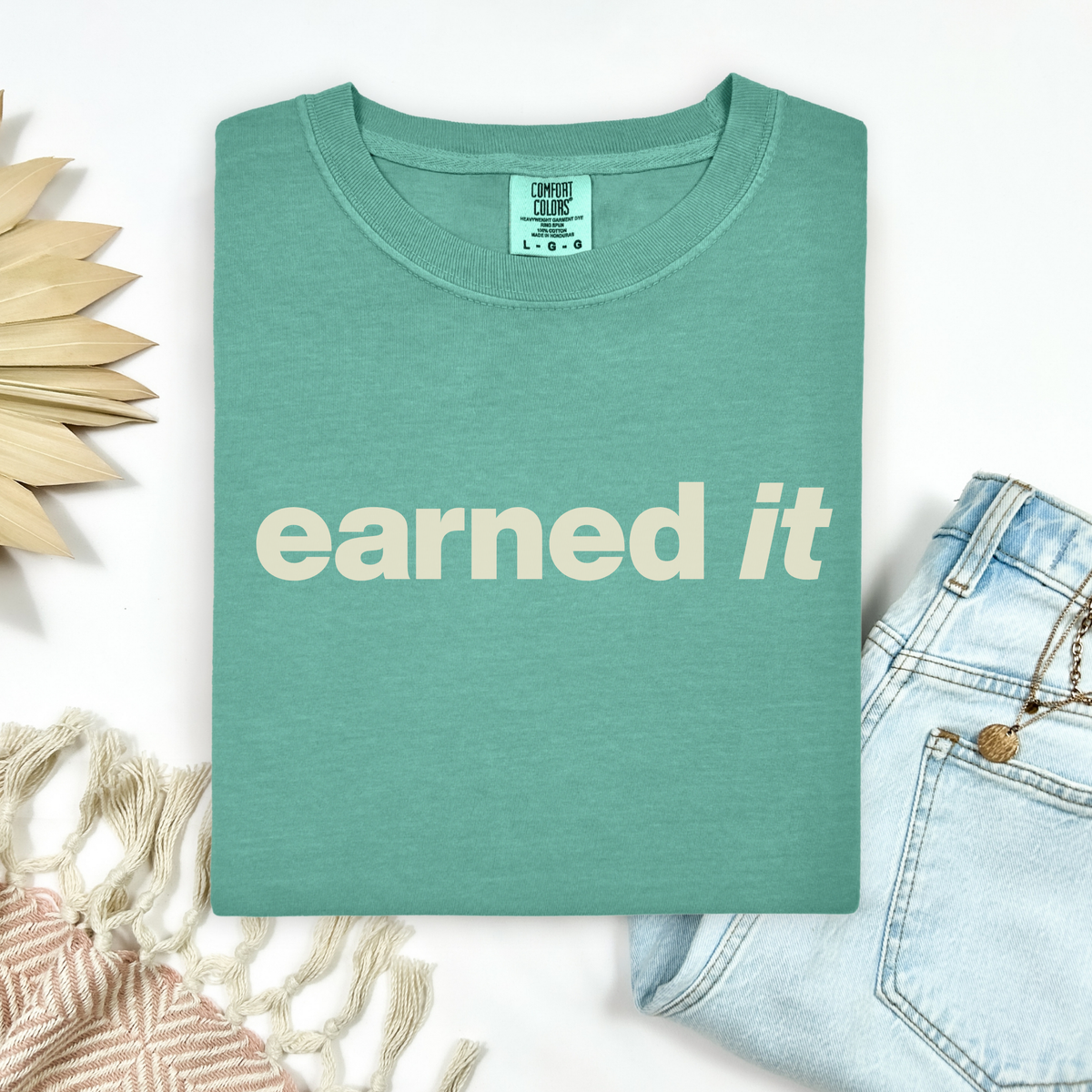 A folded light green tee shirt that says "earned it" in beige