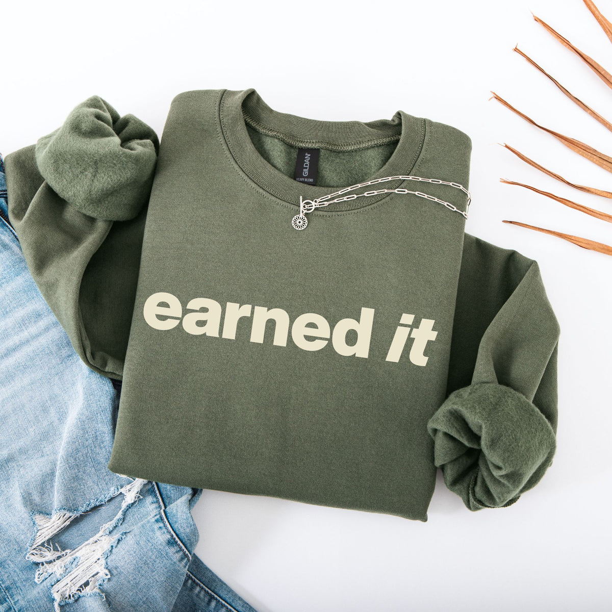 A folded  dark green sweatshirt with the words "Earned It" in a soft celery yellow font.