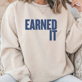 A closeup of a beige sweatshirt and jeans. The sweatshirt says 