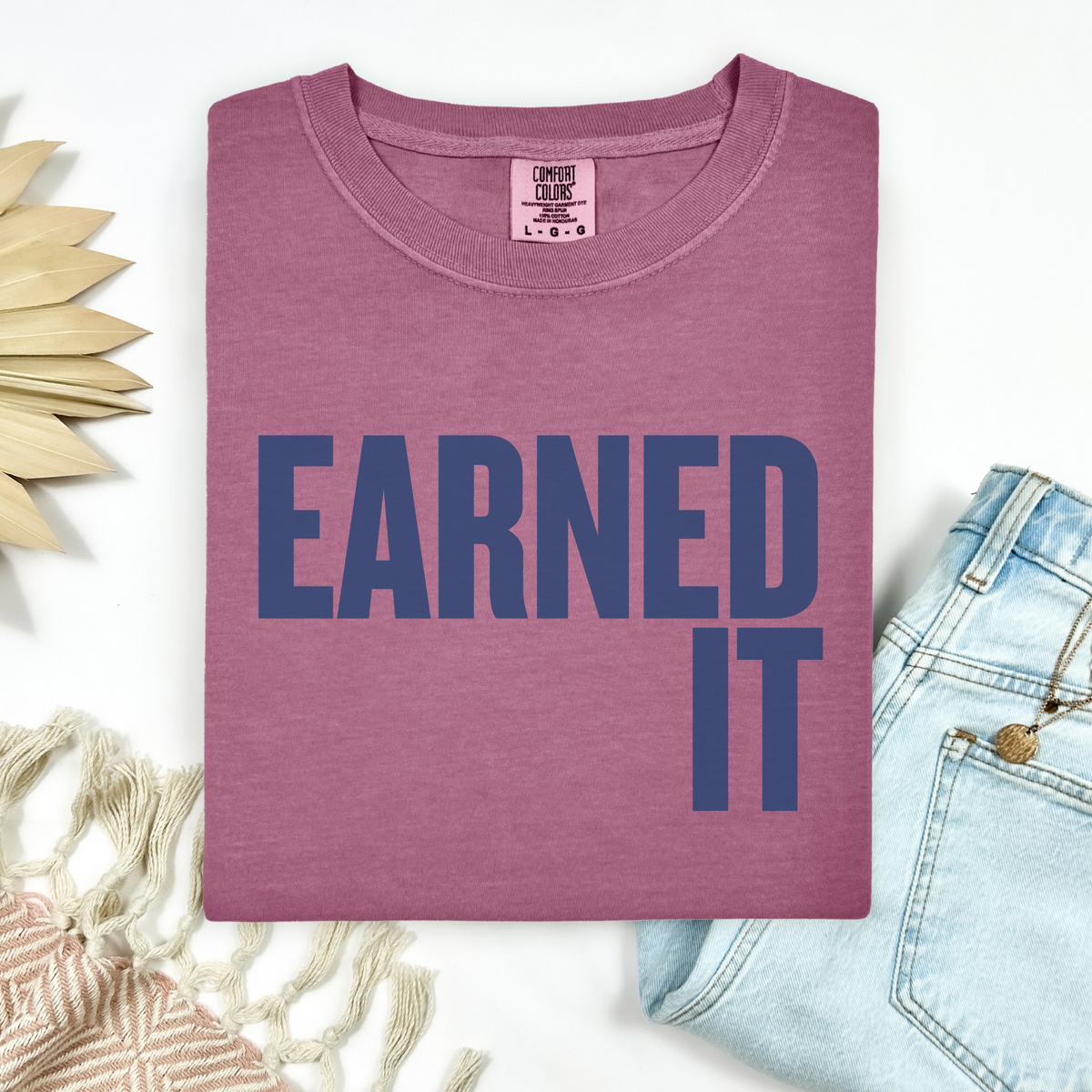 A berry colored Comfort Colors t-shirt that says "Earned It" in navy blue.
