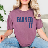 Person wearing a berry pink t-shirt with 'EARNED IT' text, sitting on a couch.