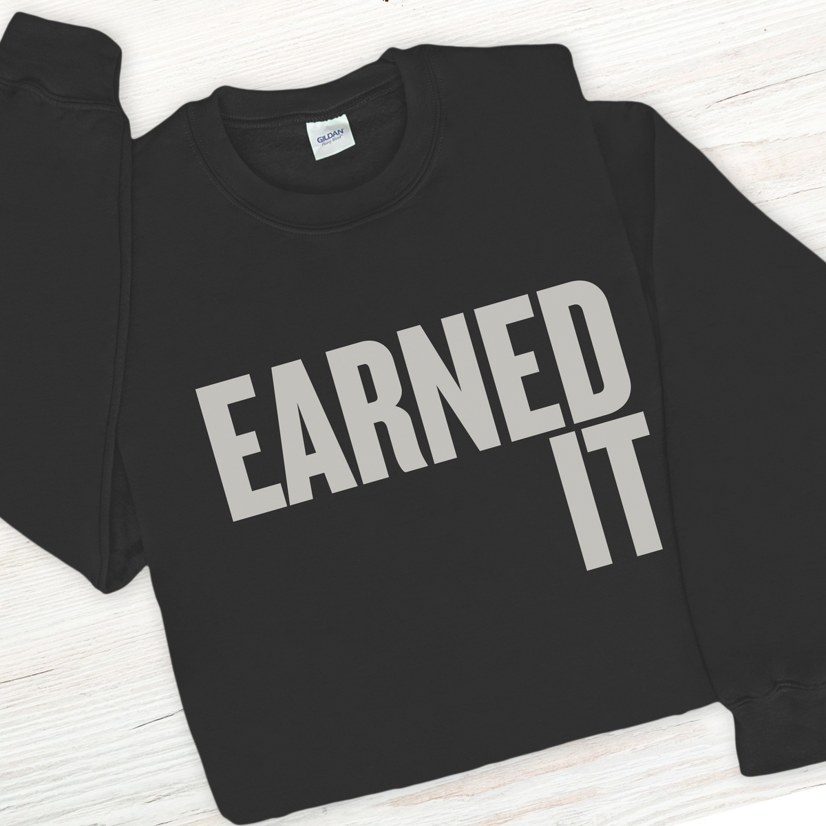 Black sweatshirt with 'Earned It' text on a white wooden surface