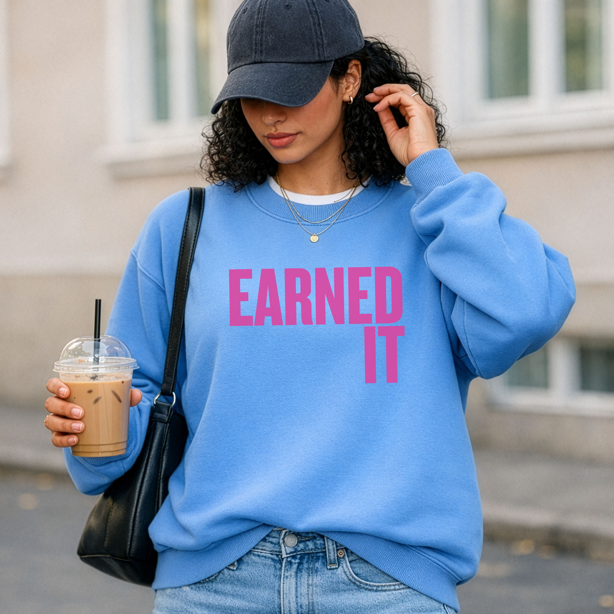 Woman wearing a blue sweatshirt with 'EARNED IT' text, holding a drink.