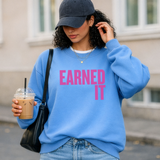 Woman wearing a blue sweatshirt with 'EARNED IT' text, holding a drink.