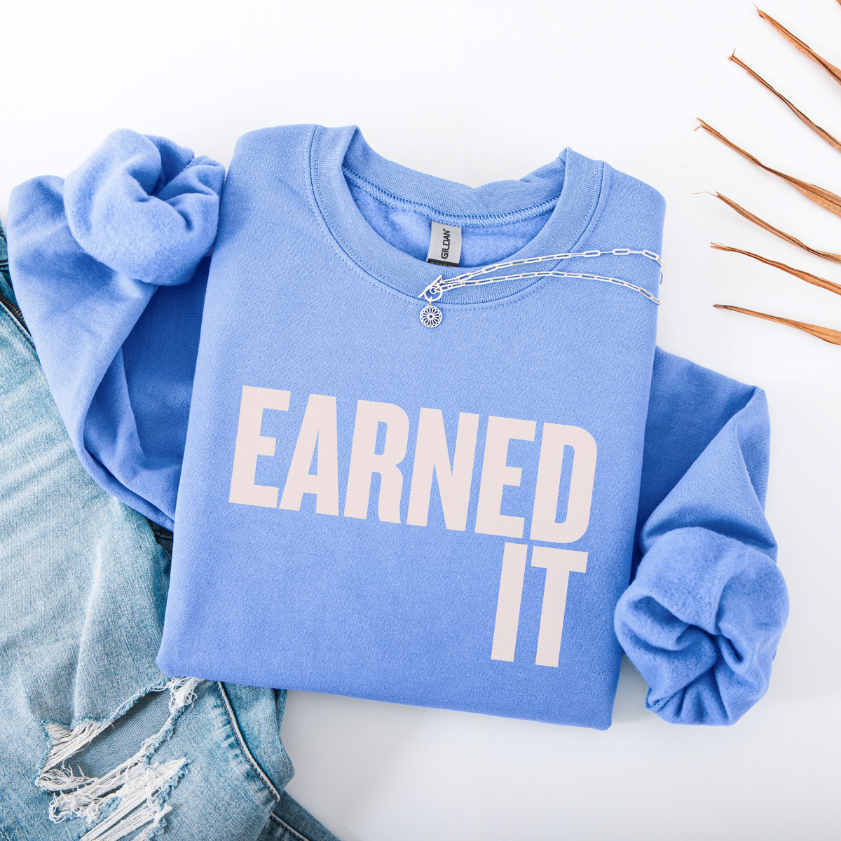 A folded light blue sweatshirt with the words "Earned It" in soft pink font.
