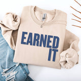 A folded beige sweatshirt and jeans. The sweatshirt says 