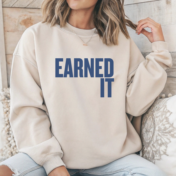Person wearing a beige sweatshirt with 'Earned It' text in blue.