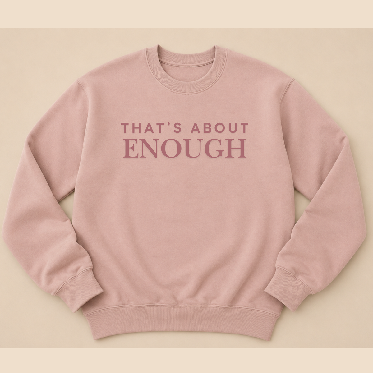 A dusty pink crewneck sweatshirt with the text 'THAT'S ABOUT ENOUGH' printed in a matching muted pink font across the chest, displayed flat against a solid beige background.
