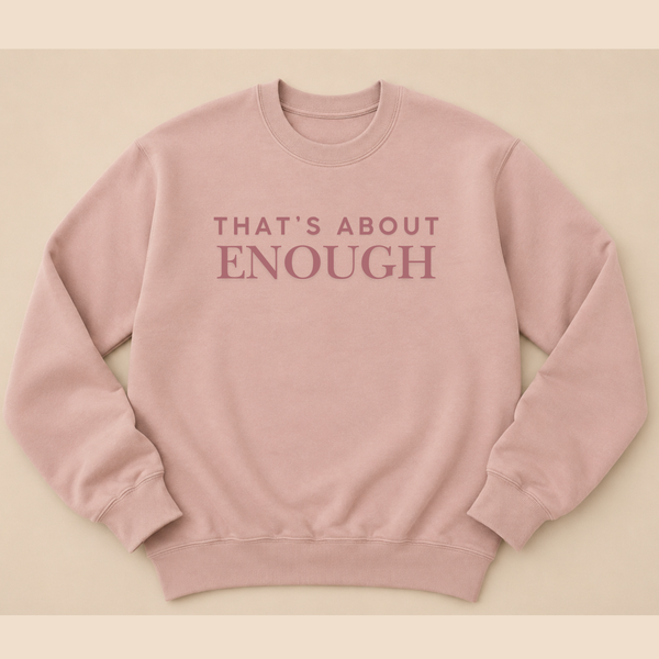 A dusty pink crewneck sweatshirt with the text 'THAT'S ABOUT ENOUGH' printed in a matching muted pink font across the chest, displayed flat against a solid beige background.