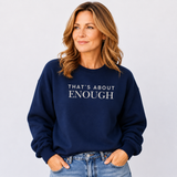 A woman wearing a navy blue crewneck sweatshirt with the text 'THAT'S ABOUT ENOUGH' printed in white across the chest, paired with light-wash blue jeans, set against a plain light gray background.