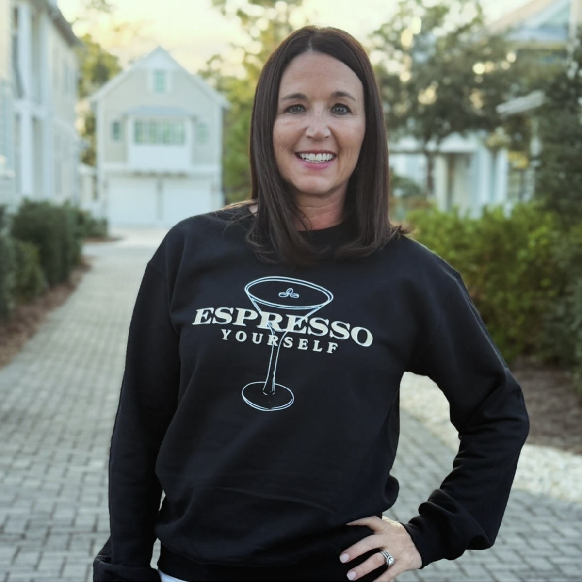 Woman wearing a black sweatshirt with 'Espresso Yourself' text and a coffee cup graphic.