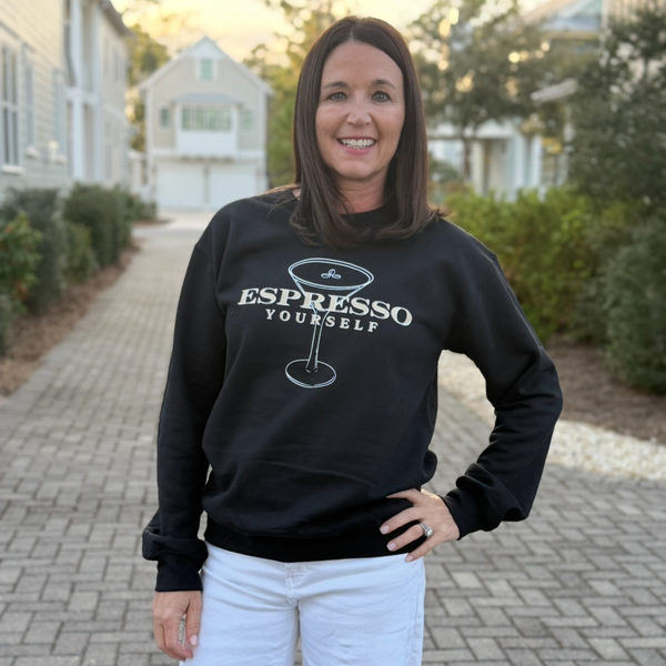 Woman wearing a black sweatshirt with 'Espresso Yourself' text and a coffee cup graphic, standing outdoors.
