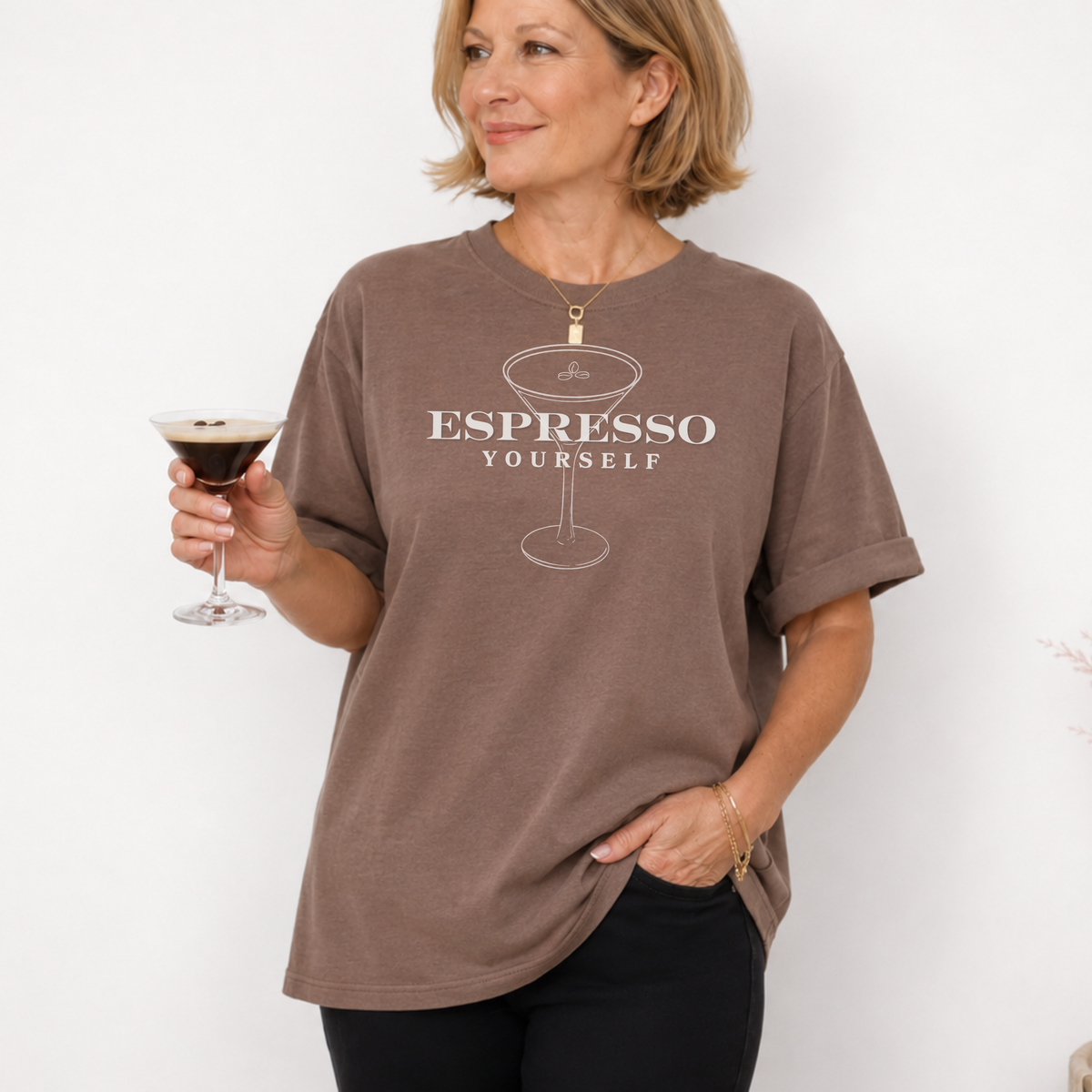Woman wearing a brown t-shirt with 'Espresso Yourself' text, holding a glass of dark liquid.