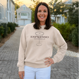 Woman wearing a beige sweatshirt with 'Espresso Yourself' text and a martini glass graphic, standing outdoors.