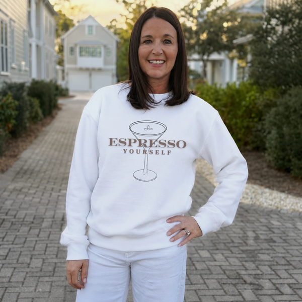 Woman wearing a white sweatshirt with 'Espresso Yourself' text, standing outdoors.