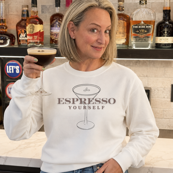 Woman holding a glass of espresso martini in a bar setting, wearing a sweatshirt with 'Espresso Yourself' text.
