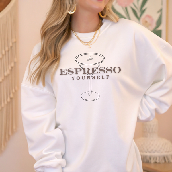 White sweatshirt with 'Espresso Yourself' text and martini glass graphic worn by a person.