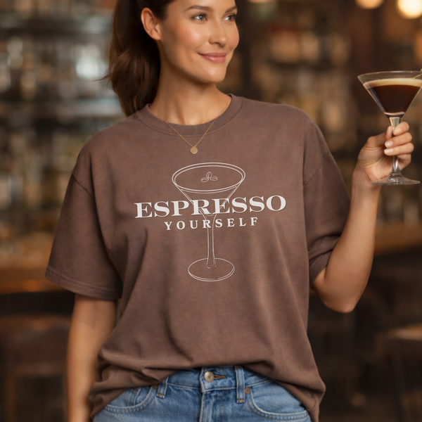 Woman wearing a brown t-shirt with 'Espresso Yourself' design, holding a martini glass in a bar setting.