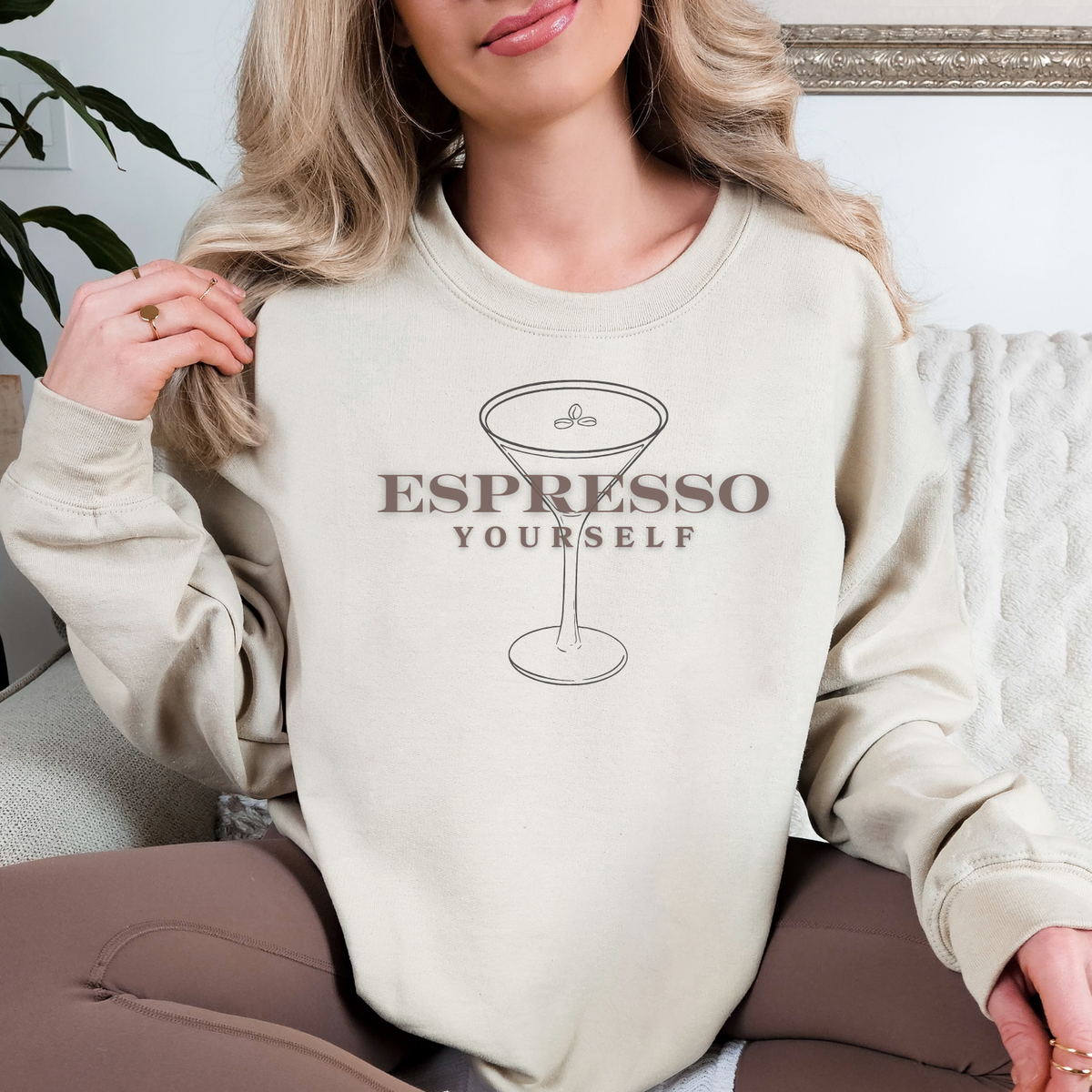 Person wearing a beige sweatshirt with 'Espresso Yourself' text and martini glass graphic.