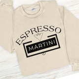 Beige sweatshirt with 'Espresso Martini' text design on a light wooden surface