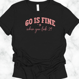 Black t-shirt with pink text '60 is fine when you look 29' on a white marble background