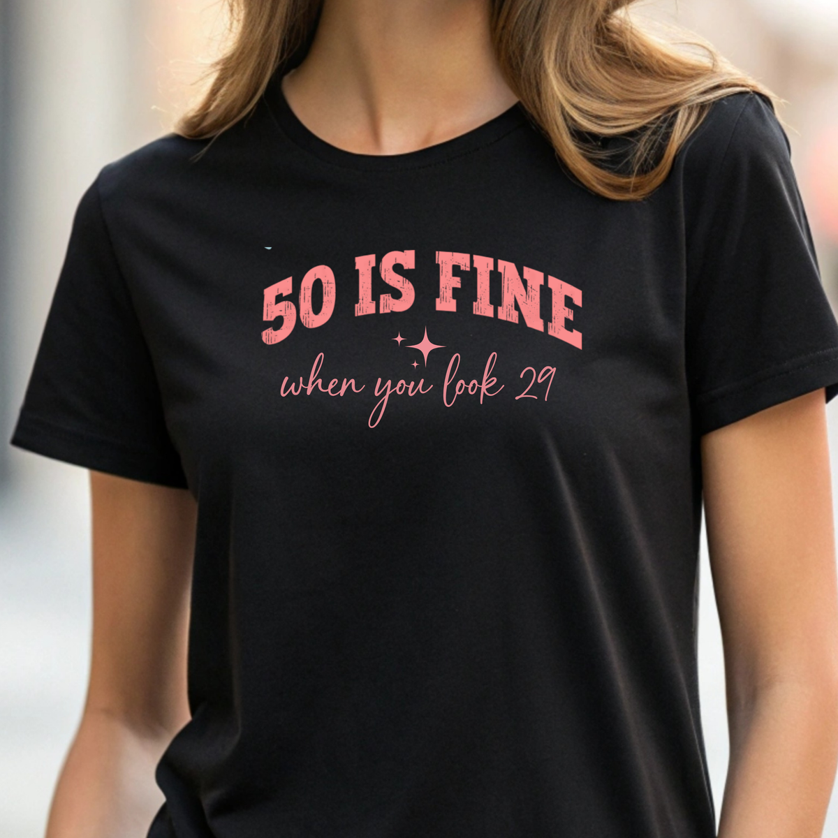 Person wearing a black t-shirt with pink text '50 IS FINE when you look 29'.