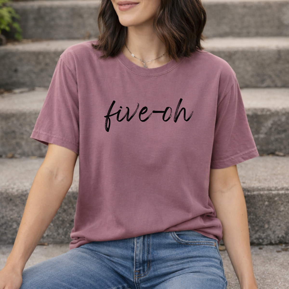 A woman wearing a purple berry t-shirt with 'five-oh' text sitting on steps.