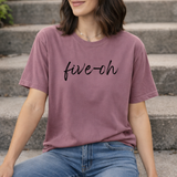 A woman wearing a purple berry t-shirt with 'five-oh' text sitting on steps.