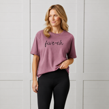Woman wearing a berry purple 'five-oh' t-shirt against a white paneled wall
