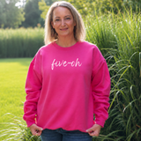 A woman wearing a bright pink crewneck sweatshirt with 'five-oh' written in white script across the chest, standing outdoors in a grassy park setting.
