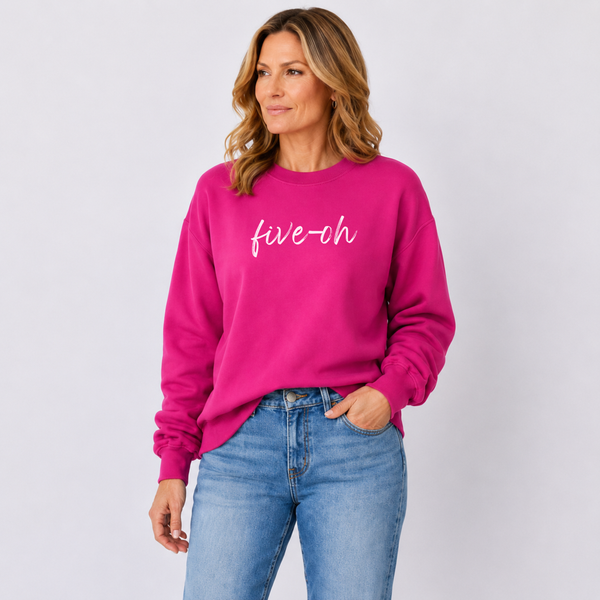 Woman wearing a bright pink sweatshirt with 'five-ch' text and blue jeans on a light gray background
