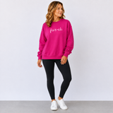 Woman wearing a bright pink sweatshirt with 'five-oh' text, black leggings, and white sneakers on a light gray background.