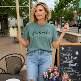 Woman wearing a green t-shirt with 'five-oh' text, holding a drink, standing outdoors.