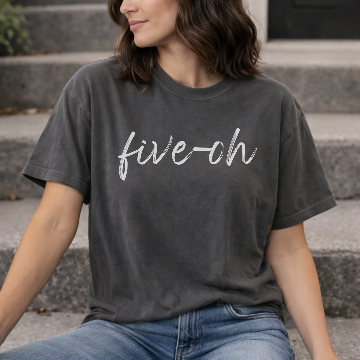 Person wearing a dark gray t-shirt with 'five-oh' printed on it, sitting on steps.