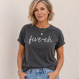 Woman wearing a dark gray t-shirt with 'five-oh' text against a beige background