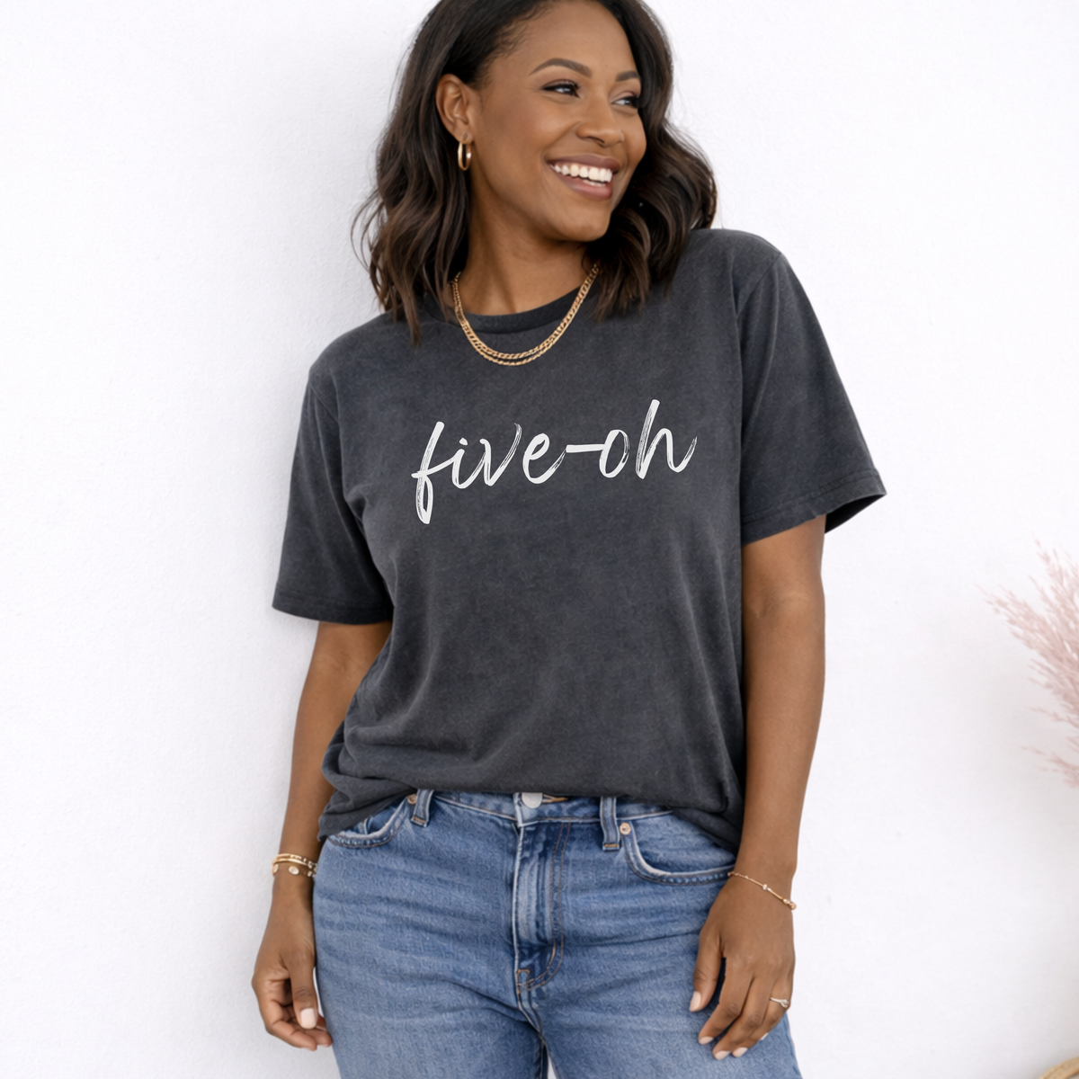 Woman wearing a dark gray t-shirt with 'five-oh' text and blue jeans against a white background