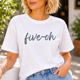 A woman wearing a white t-shirt with 'five-oh' text, sitting outdoors.