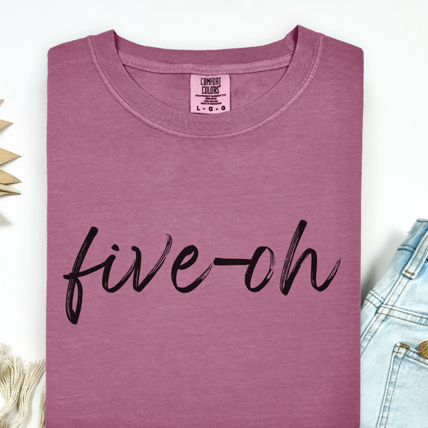 Folded mauve t-shirt with 'five-oh' text on a light background