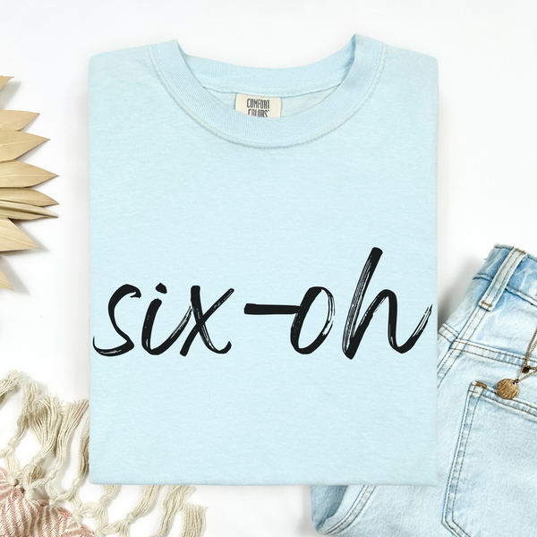 Light blue sweatshirt with 'six-oh' text, displayed with denim jeans and decorative elements.