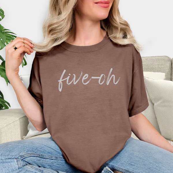 Person wearing a brown t-shirt with 'five-oh' text, sitting on a couch.