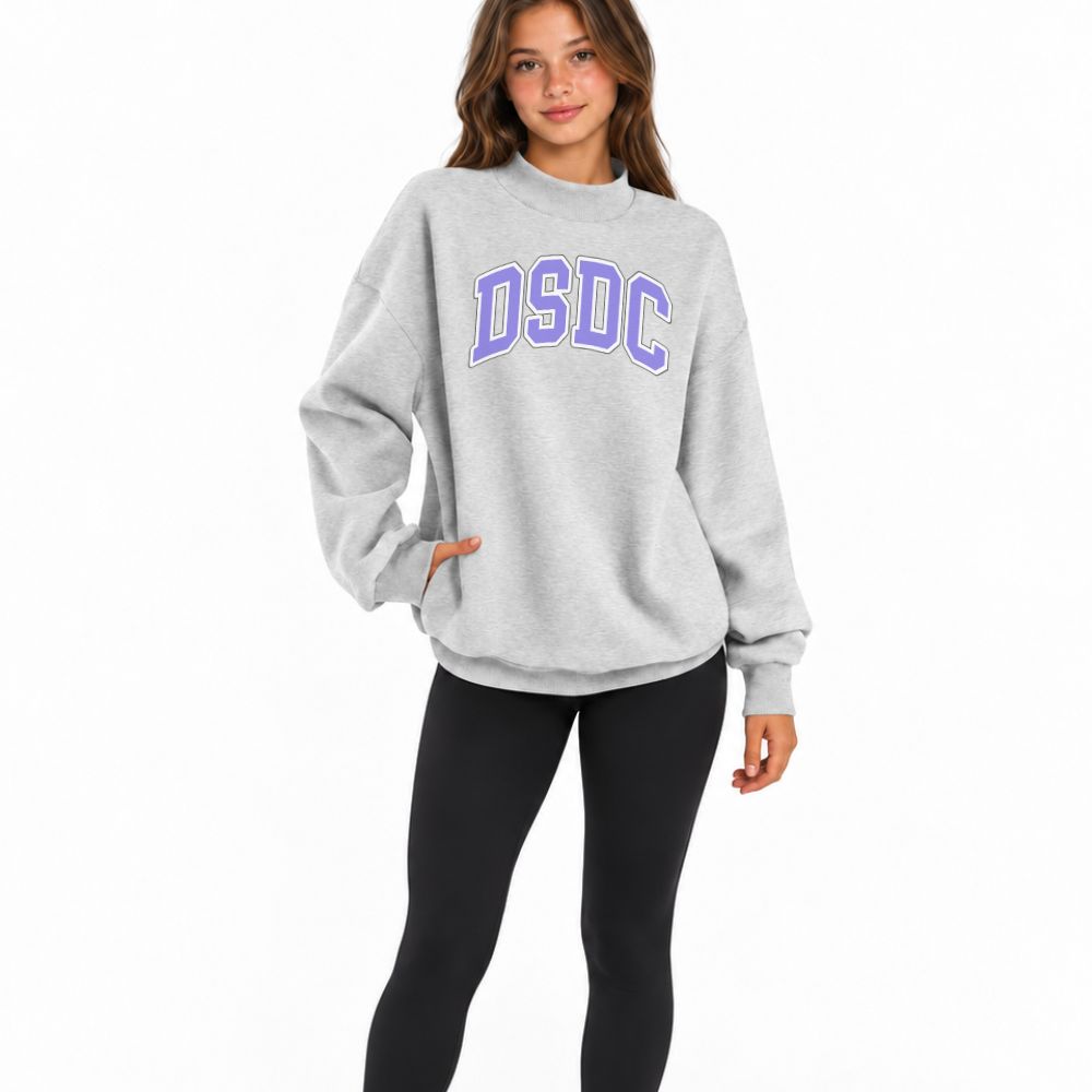 A woman modeling a light gray crewneck sweatshirt with 'DSDC' printed in purple varsity letters across the chest, paired with black leggings, against a plain white background.