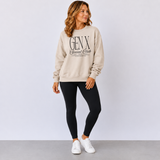 A woman modeling a beige crewneck sweatshirt with 'GEN X Social Club' printed in black on the front, paired with black leggings and white sneakers, against a light gray studio background.