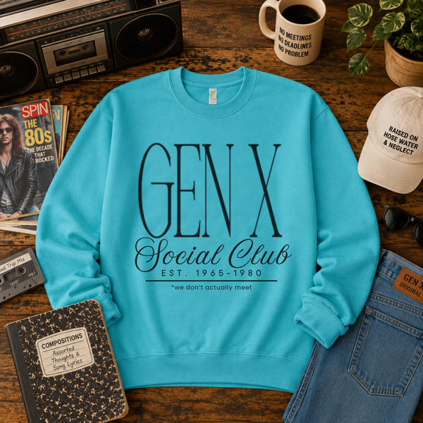 A turquoise crewneck sweatshirt with 'GEN X Social Club' printed in black on the front, styled in a retro-themed flat lay on a wooden table with a cassette tape, coffee mug, notebook, and denim accessories.