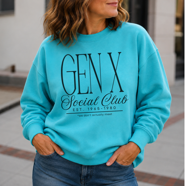A woman wearing a bright turquoise crewneck sweatshirt with a black graphic print that reads 'GEN X Social Club EST. 1965-1980' and 'we don't actually like', paired with blue jeans in an outdoor urban setting.