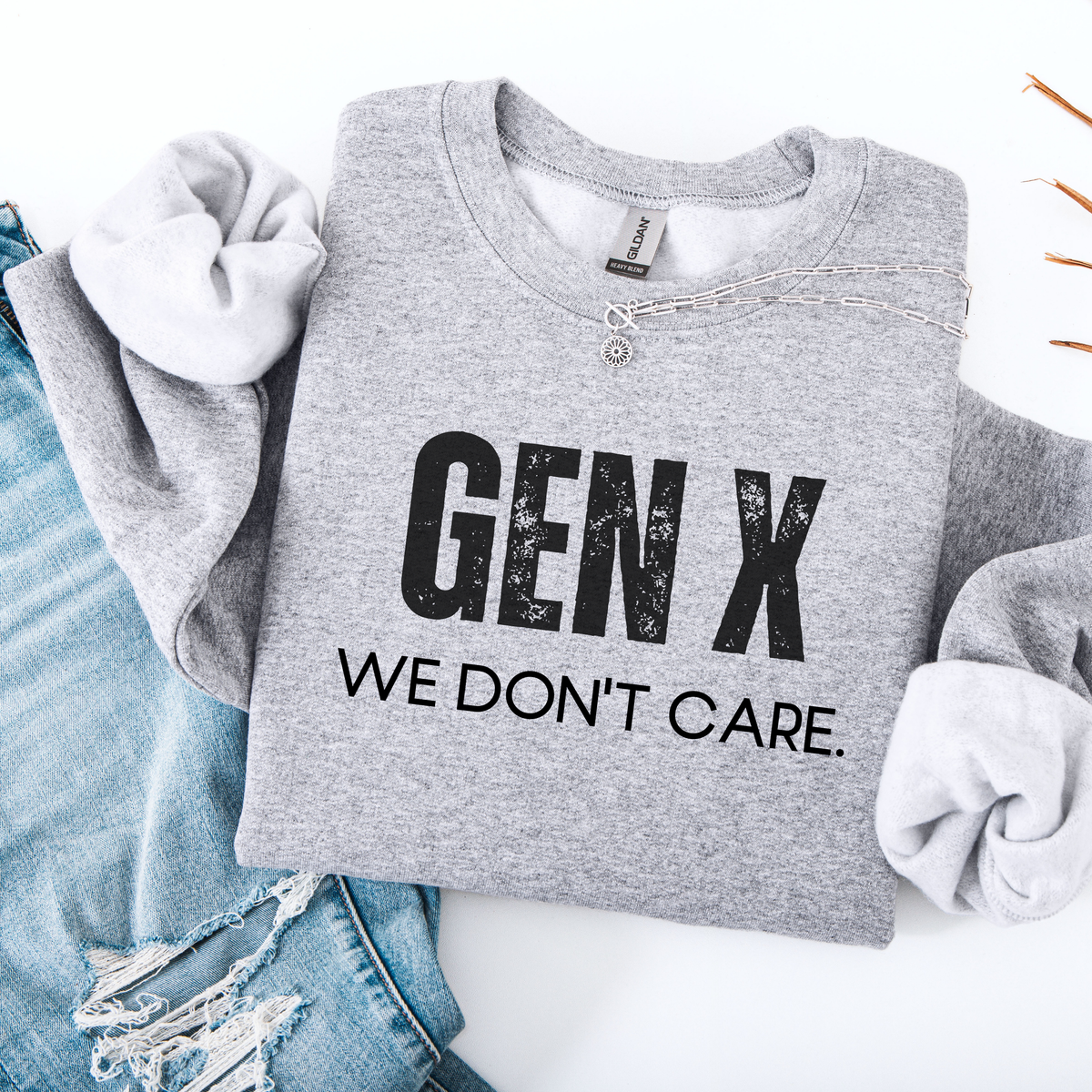 Sport Gray sweatshirt with "Gen X We Don't Care" written in distressed font folded on top of jeans.